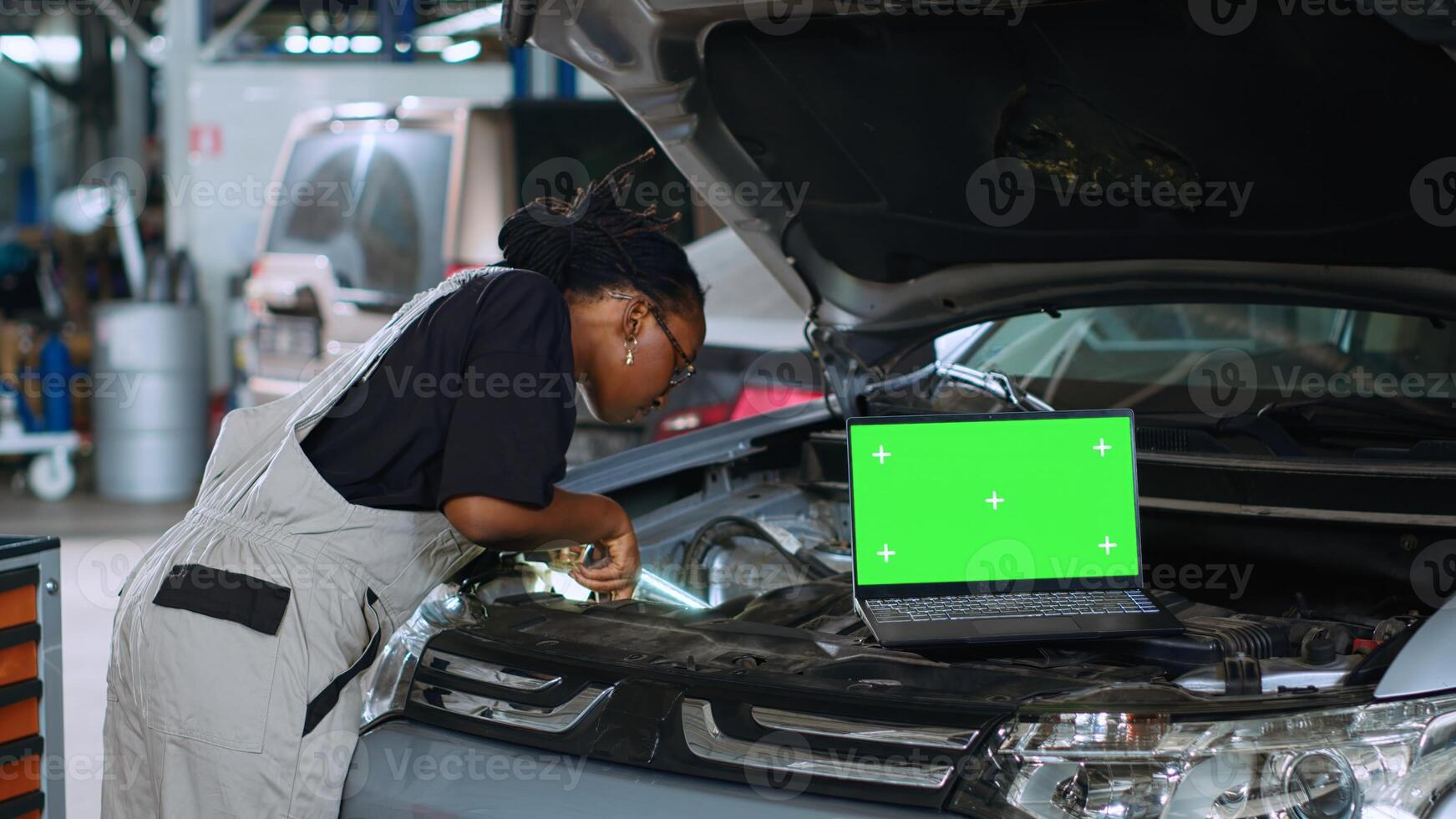 Close up shot of laptop placed on opened up car in busy garage while african american technician mends vehicle. Mockup device in repair shop with qualified employee working next to it photo