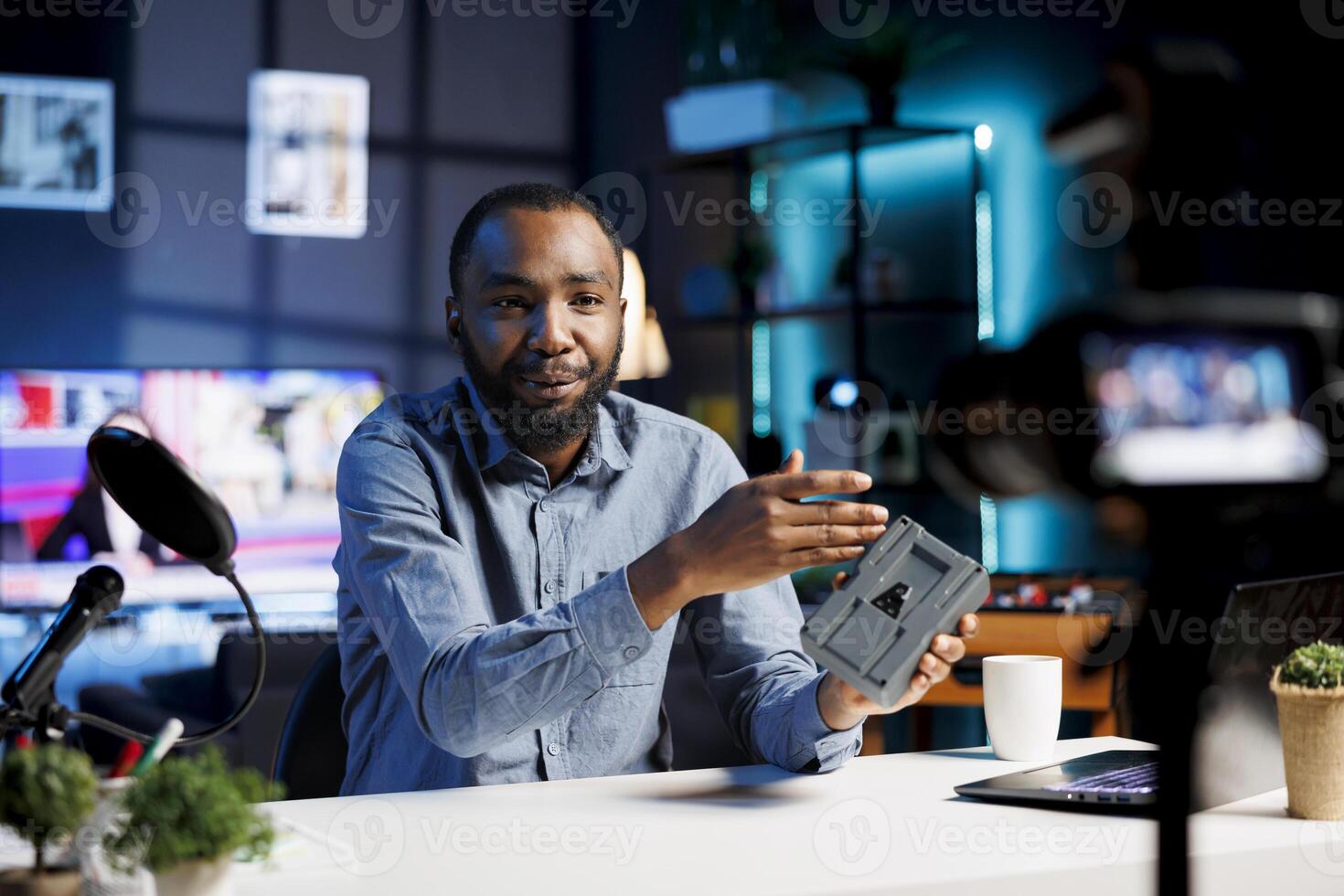 Media star reviews V mount battery powering up camera systems, comparing voltage power with other models. Tech guru filming online video, analyzing LiIon lithium accumulator photo