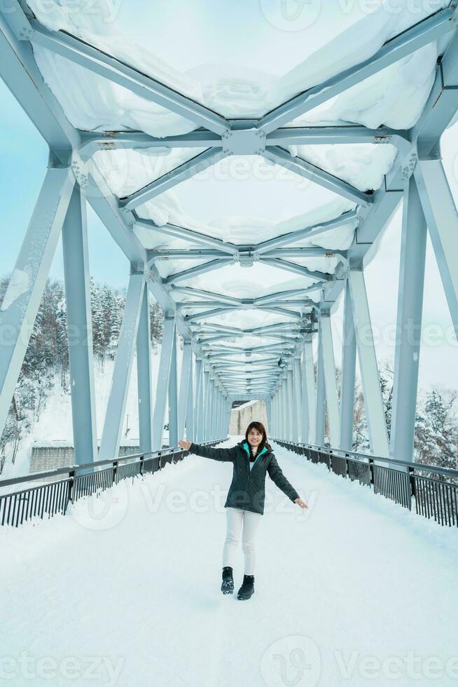 Woman tourist Visiting in Biei, Traveler in Sweater sightseeing Shirahige Waterfall bridge with Snow in winter. landmark and popular for attractions in Hokkaido, Japan. Travel and Vacation concept photo