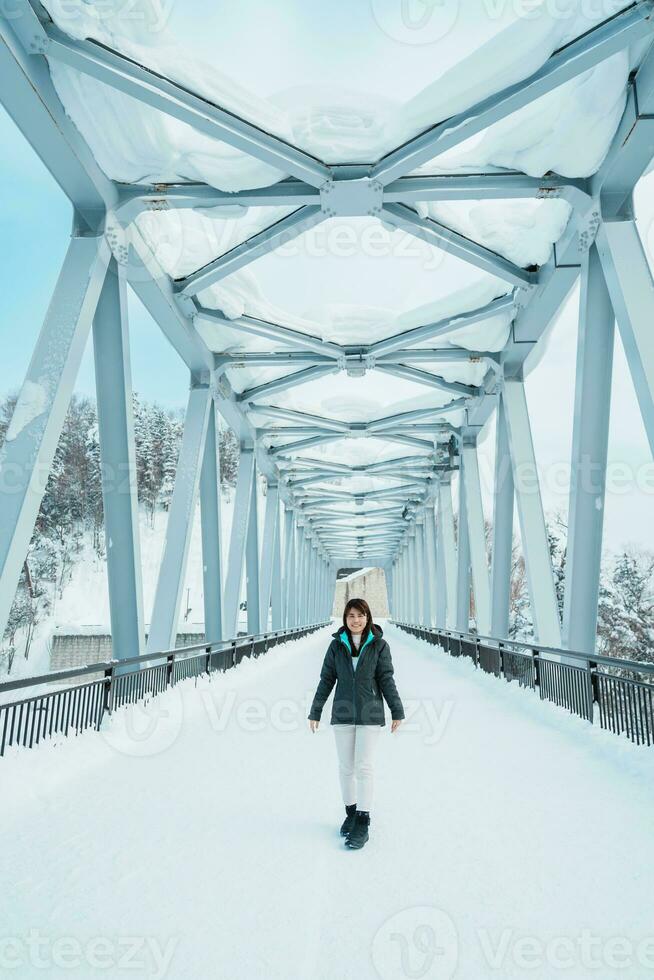 Woman tourist Visiting in Biei, Traveler in Sweater sightseeing Shirahige Waterfall bridge with Snow in winter. landmark and popular for attractions in Hokkaido, Japan. Travel and Vacation concept photo