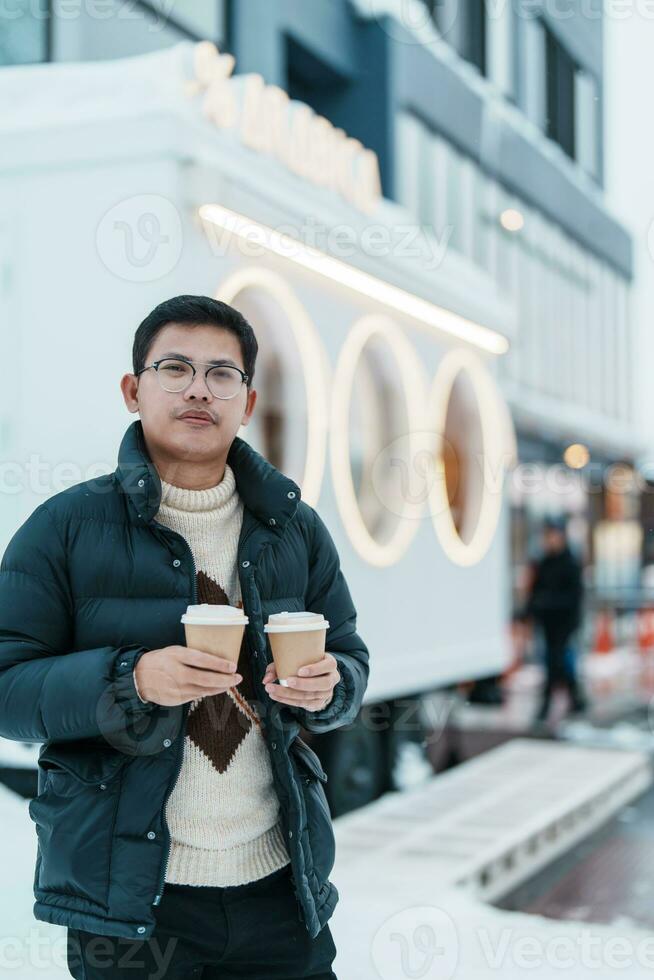 man tourist holding hot Coffee or Tea paper cup with snow in winter season during travel in Niseko. landmark and popular for attractions in Hokkaido, Japan. Travel and Vacation concepts photo