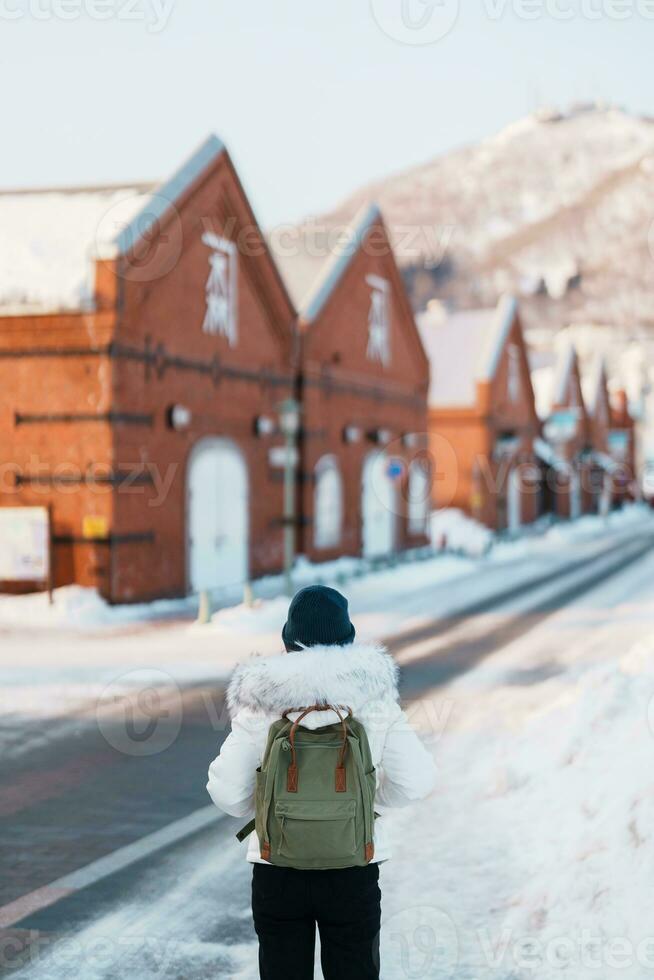 Woman tourist Visiting in Hakodate, Traveler in Sweater sightseeing Kanemori Red Brick Warehouse with Snow in winter. landmark and popular for attractions in Hokkaido,Japan.Travel and Vacation concept photo