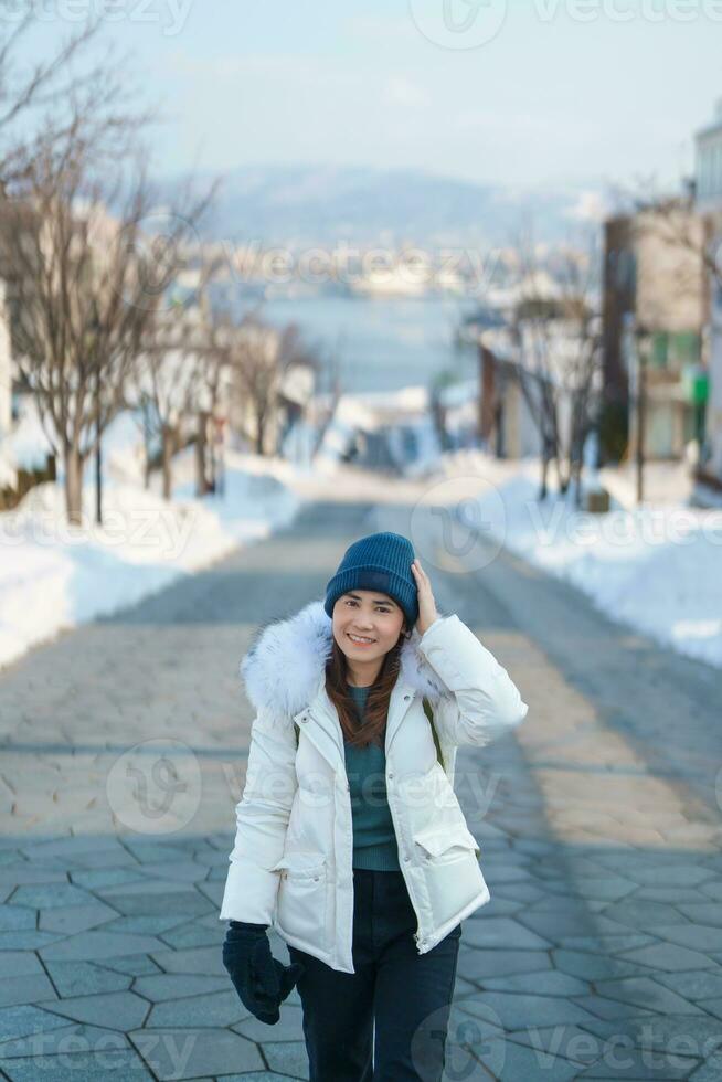 mujer turista visitando en hakodate, viajero en suéter Turismo hachiman zaka Pendiente con nieve en invierno. punto de referencia y popular para atracciones en Hokkaidō, Japón. viaje y vacaciones concepto foto