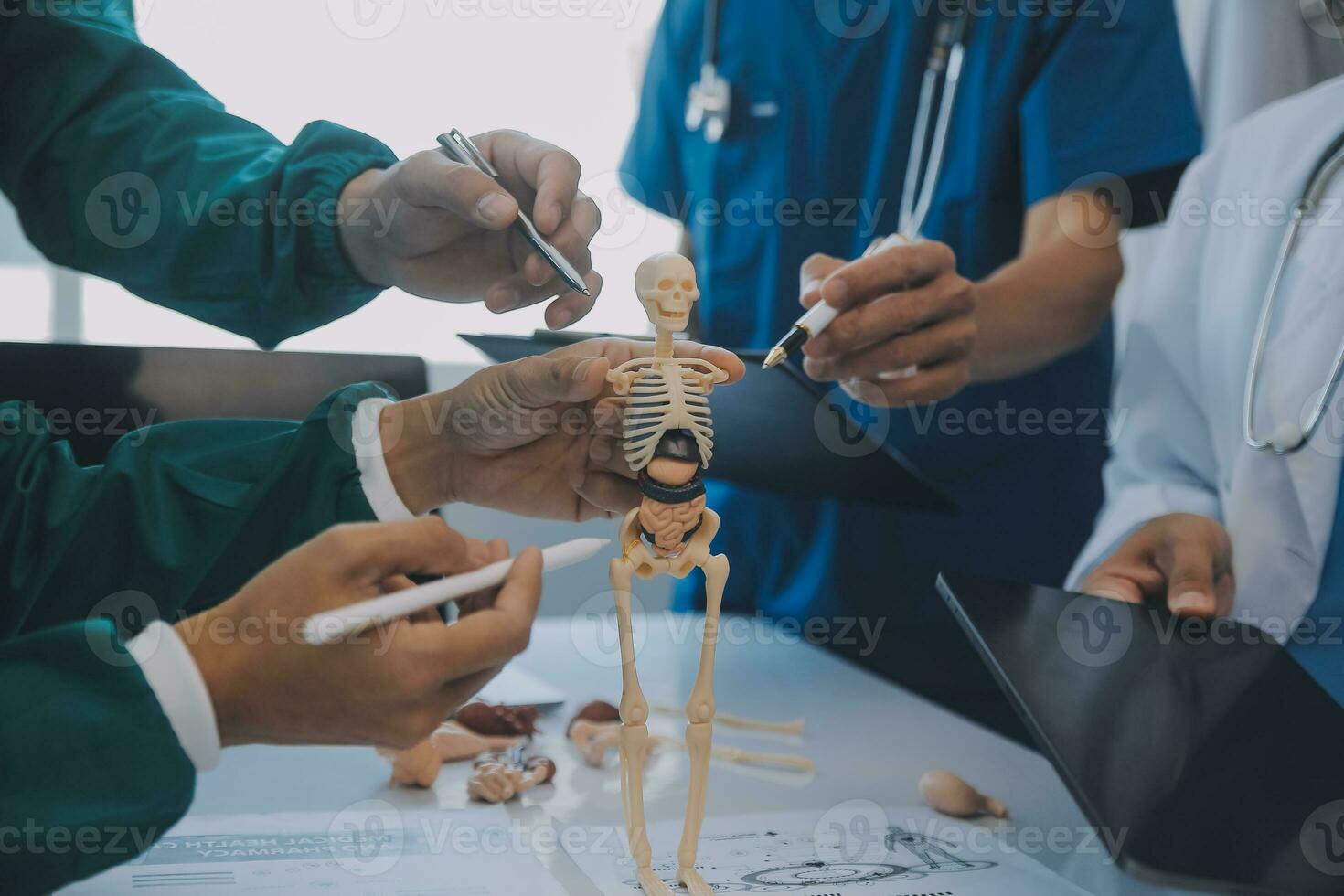 Multiracial medical team having a meeting with doctors in white lab coats and surgical scrubs seated at a table discussing a patients records photo