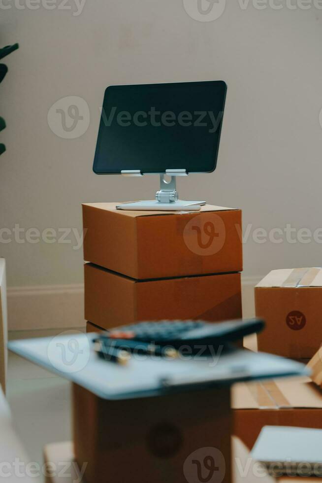 Startup SME small business entrepreneur of freelance Asian woman wearing apron using laptop and box to receive and review orders online to prepare to pack sell to customers, online sme business ideas. photo