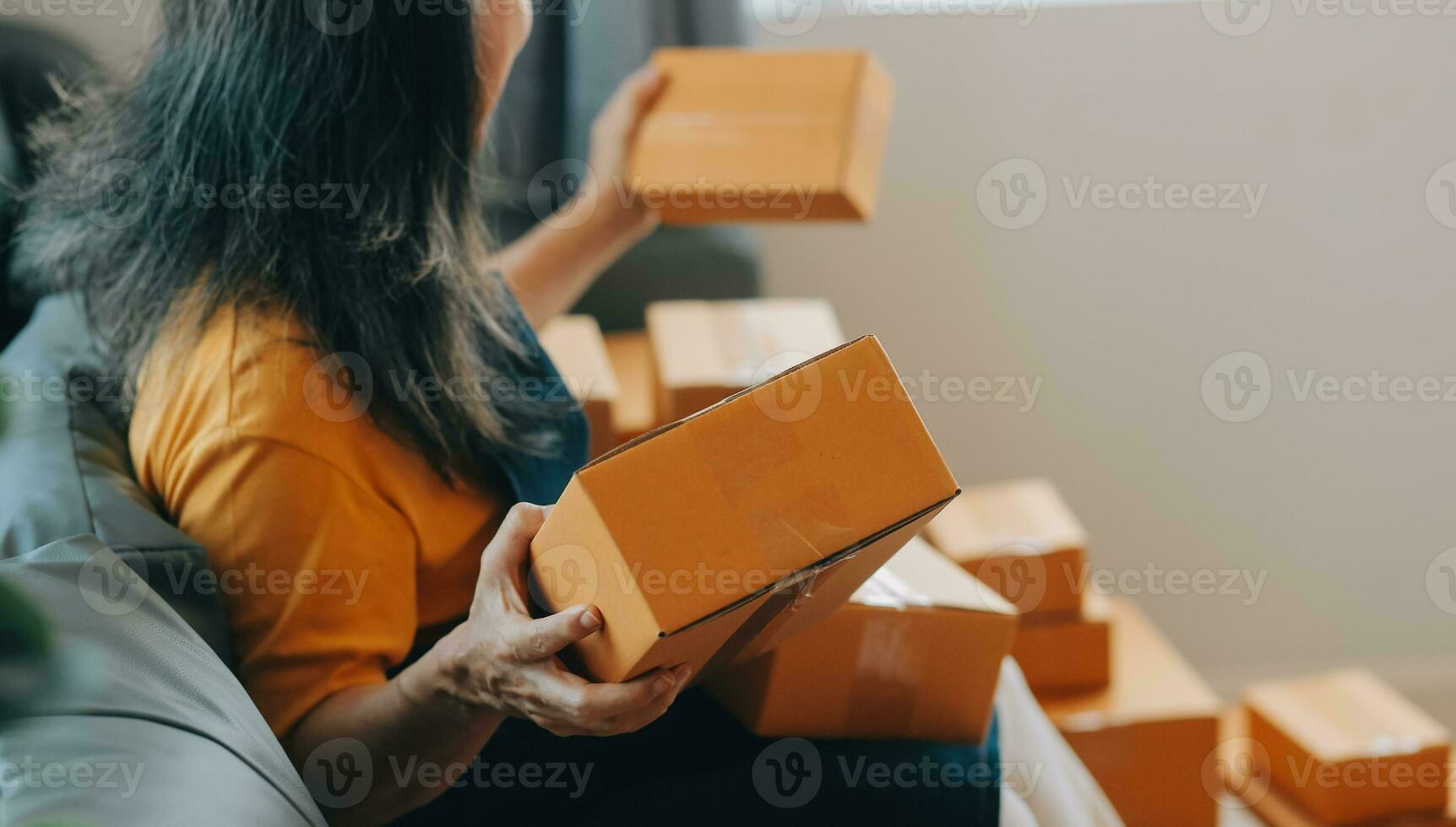 Startup SME small business entrepreneur of freelance Asian woman wearing apron using laptop and box to receive and review orders online to prepare to pack sell to customers, online sme business ideas. photo