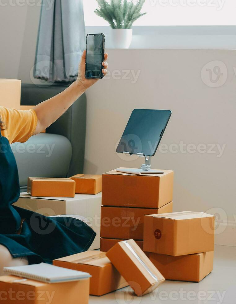 Startup SME small business entrepreneur of freelance Asian woman wearing apron using laptop and box to receive and review orders online to prepare to pack sell to customers, online sme business ideas. photo
