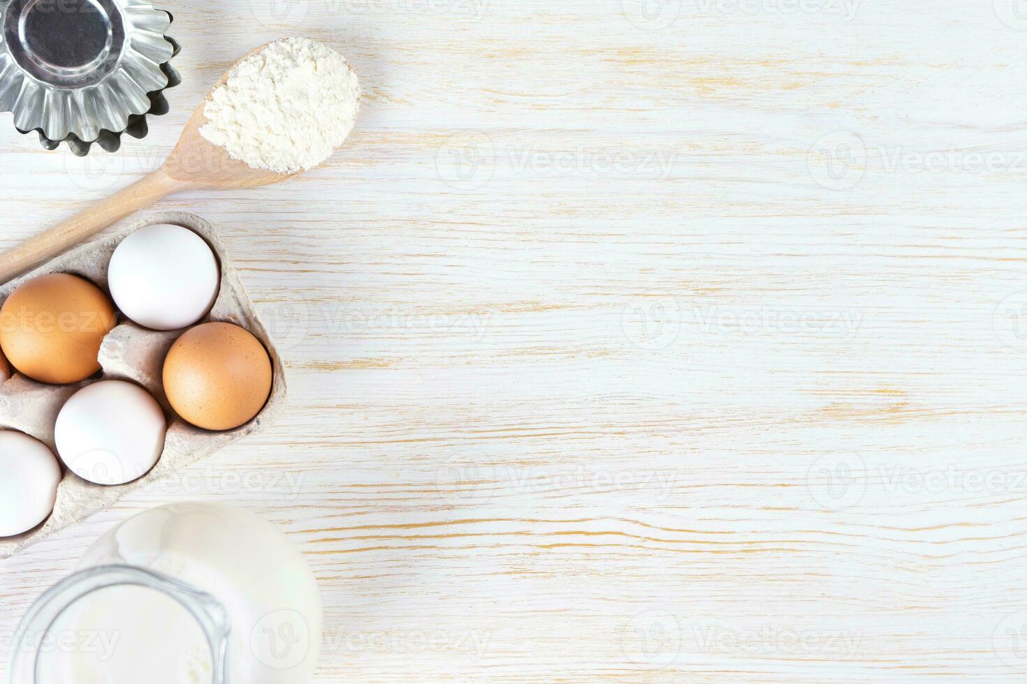 Baking ingredients flour, eggs, milk, bakeware on white wooden background with copy space photo