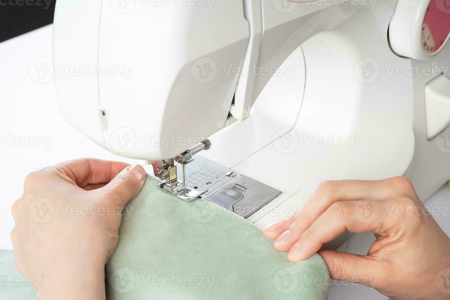 Female hands stitching white fabric on modern sewing machine at workplace in atelier photo