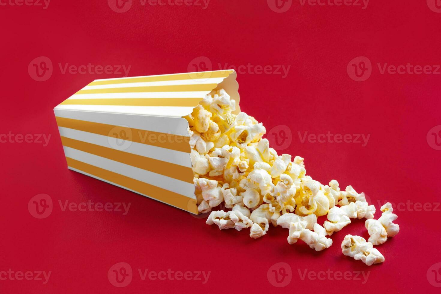 Tasty cheese popcorn falling out of a yellow striped carton bucket, isolated on red background photo