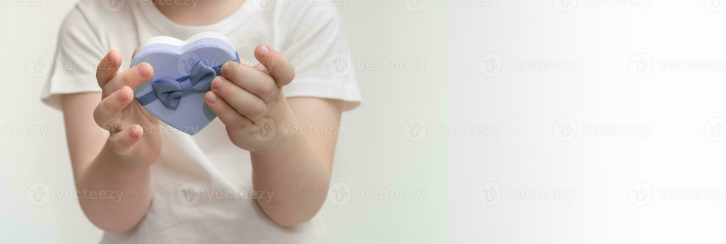 Child holds in his hands heart shaped gift box. Mothers Day, Valentines Day concept. banner, copy space. photo