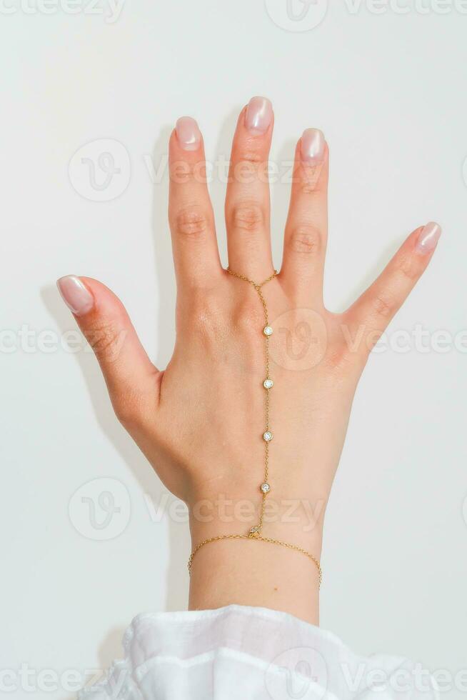 Woman hand wrist wearing golden hand chain set against a white background. photo