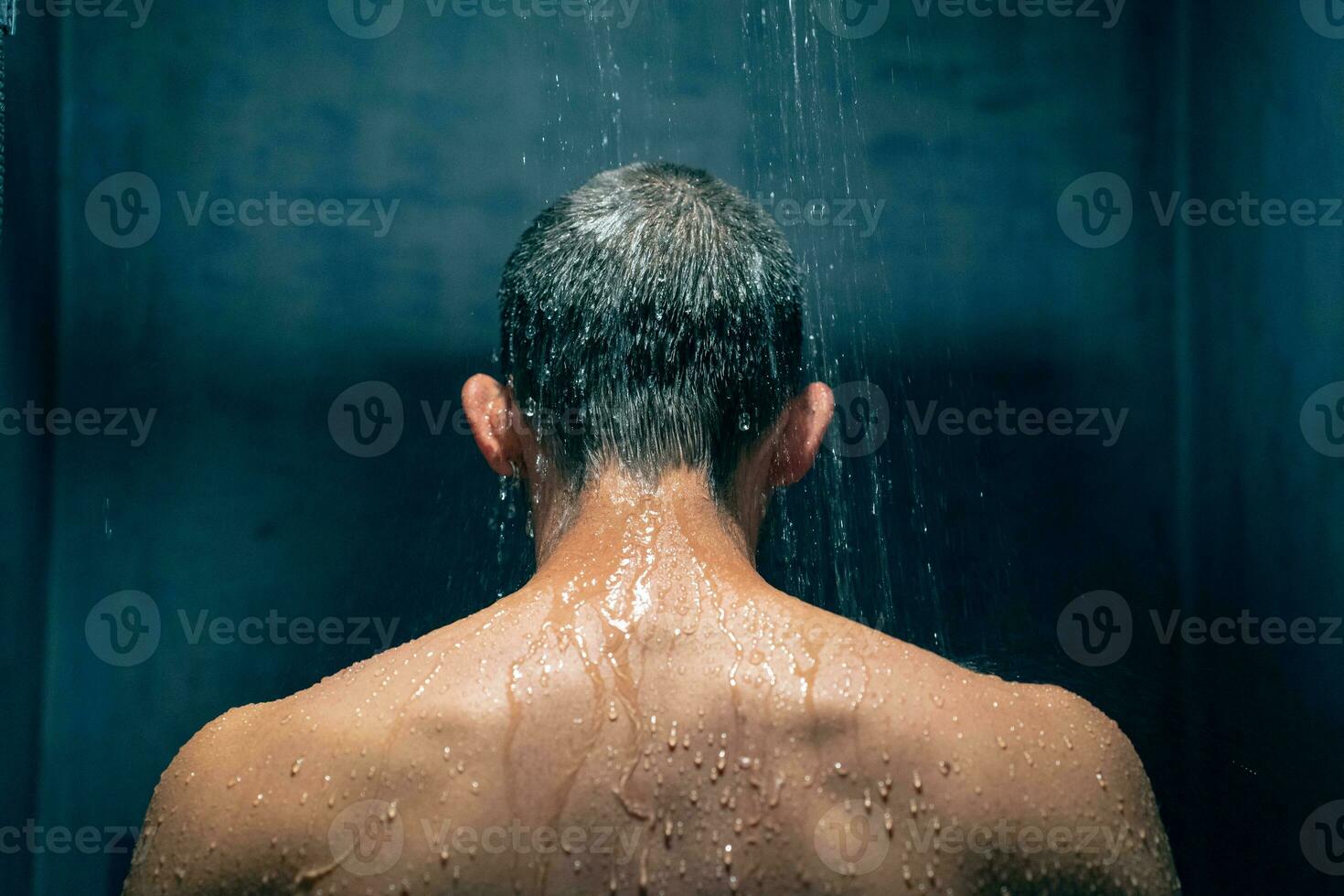 Man taking a shower relaxing under water falling from rain shower head. Guy showering body care. photo