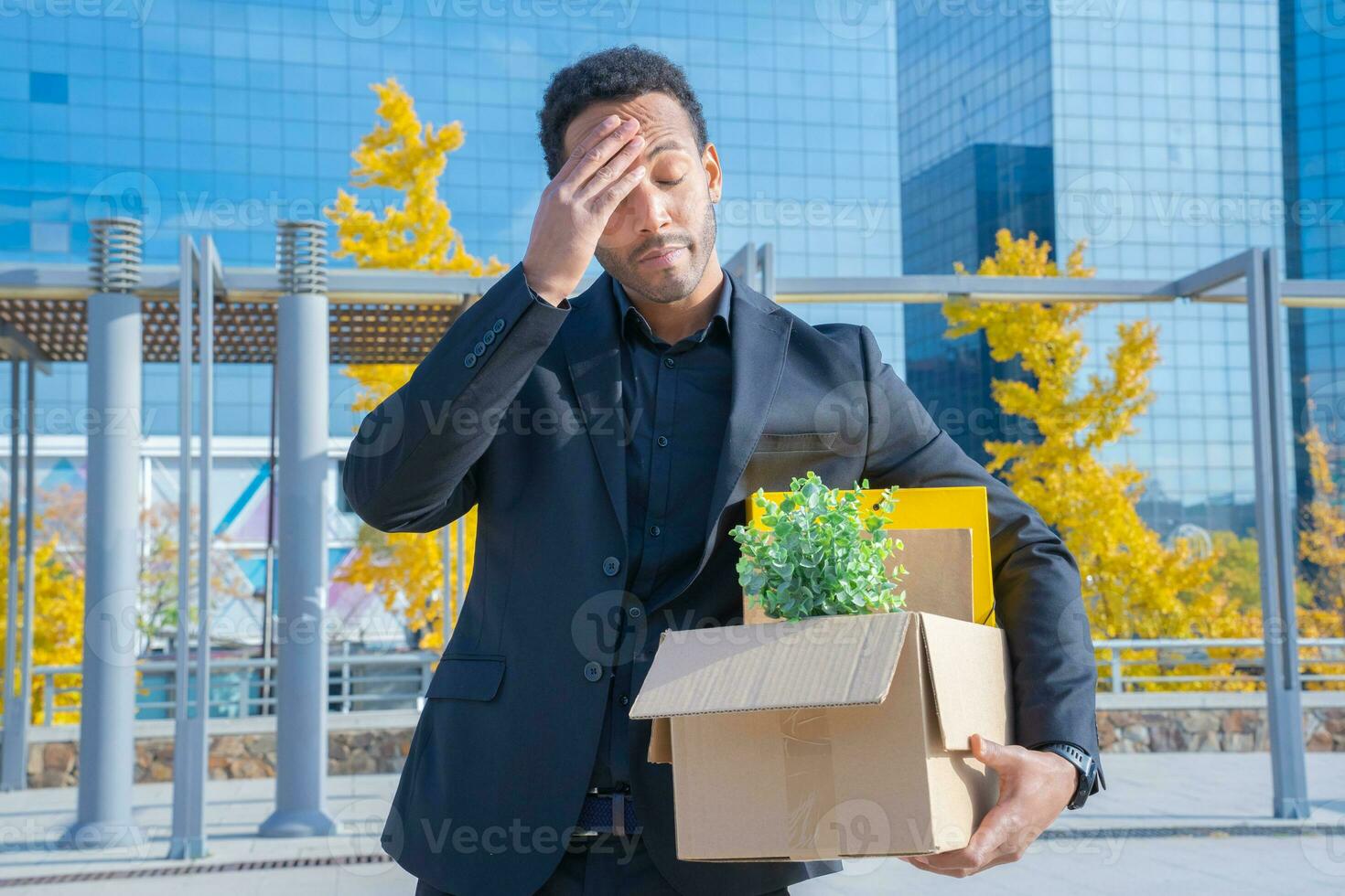 Businessman fired with cardboard box with office supplies standing sad outside office building. photo