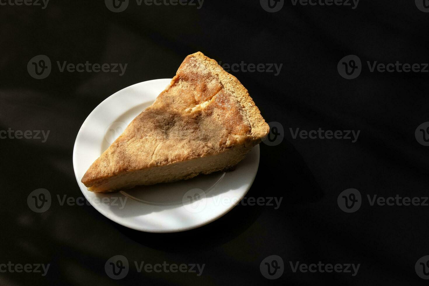 Slice of cheese pie on white plate and black background photo