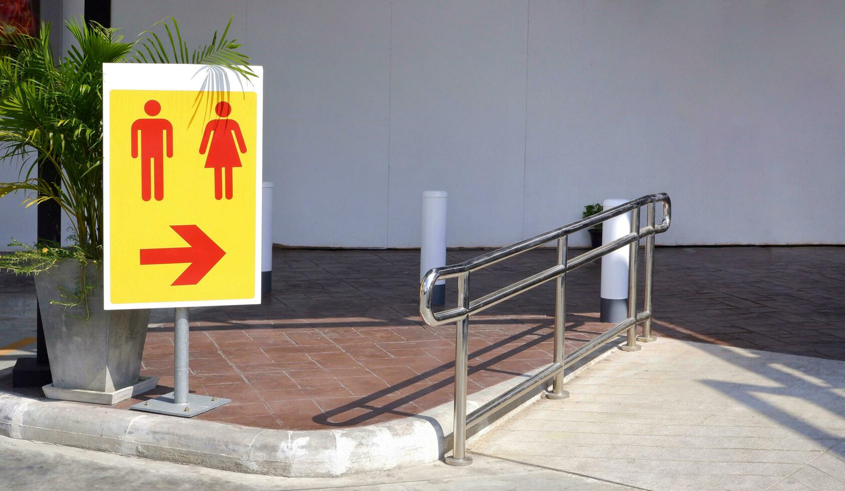 Sunlight on surface of restroom sign on metal pole with stainless steel fence on the different level ground in parking area photo