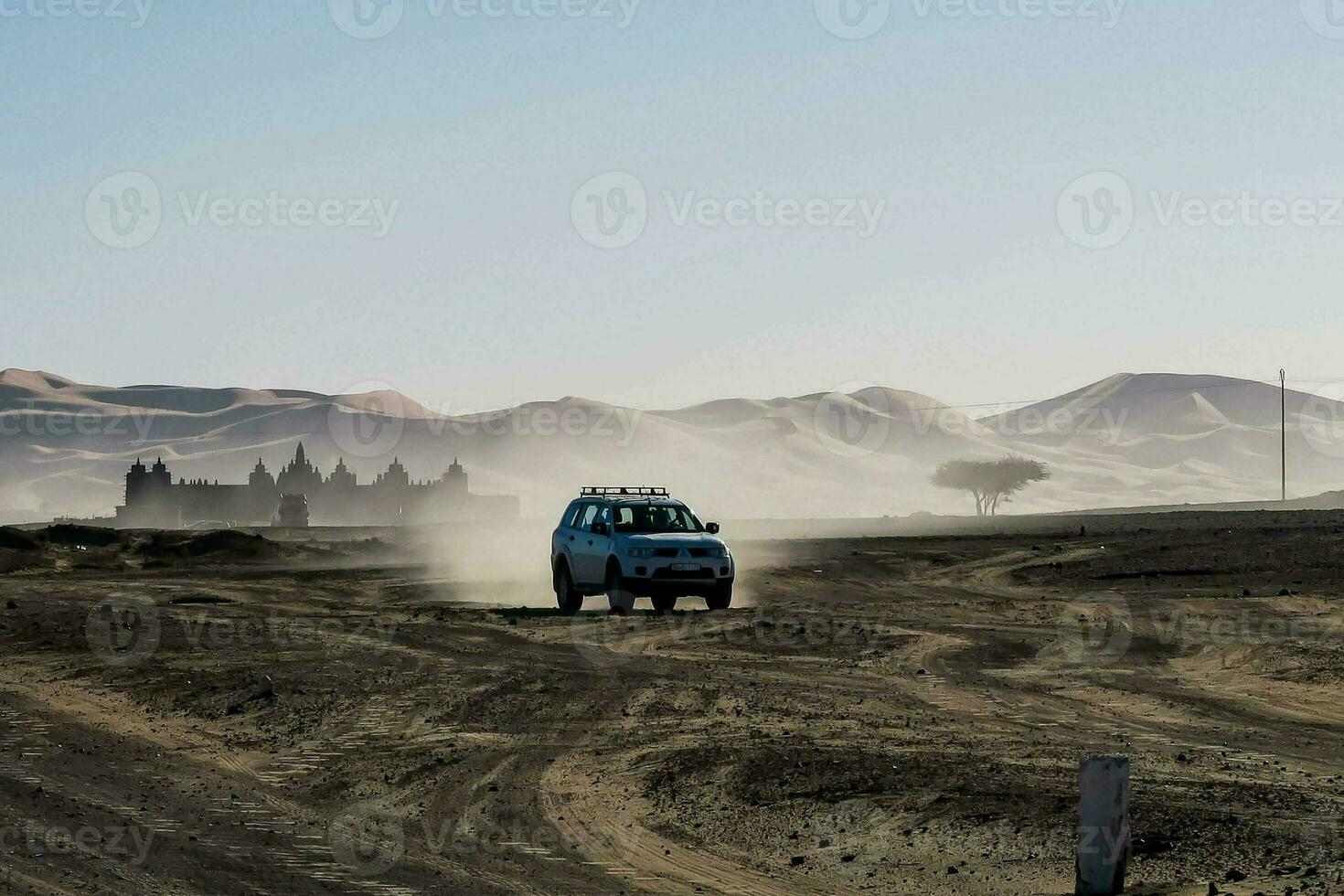 a vehicle driving through the desert with sand dunes in the background photo