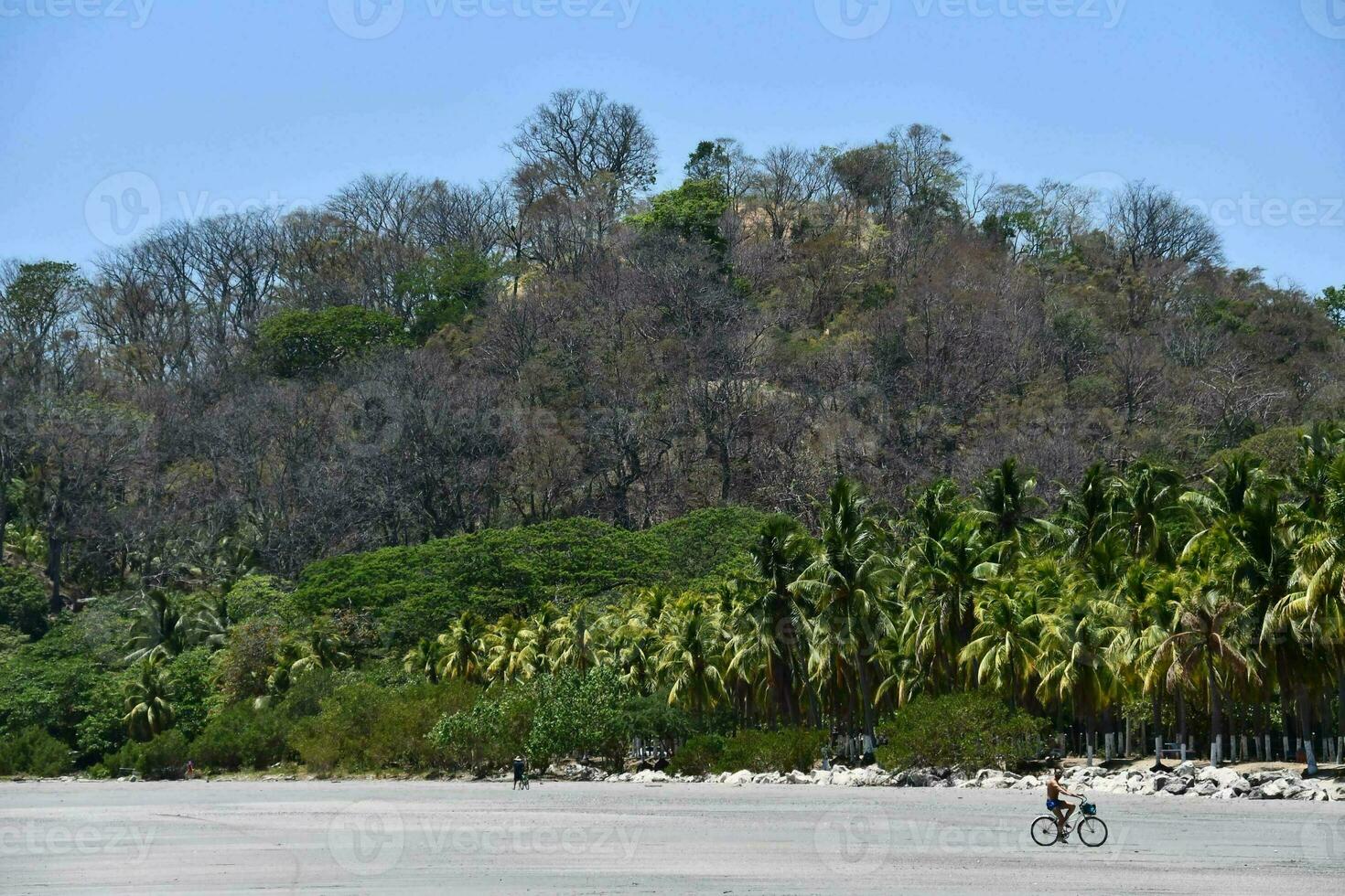 a man riding a bike on a beach near a hill photo