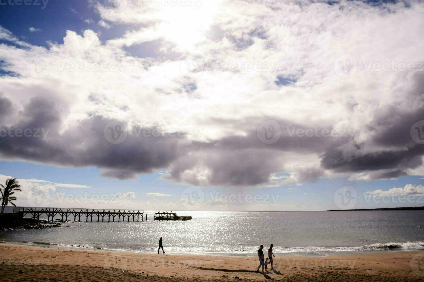 two people walk along the beach under a cloudy sky photo