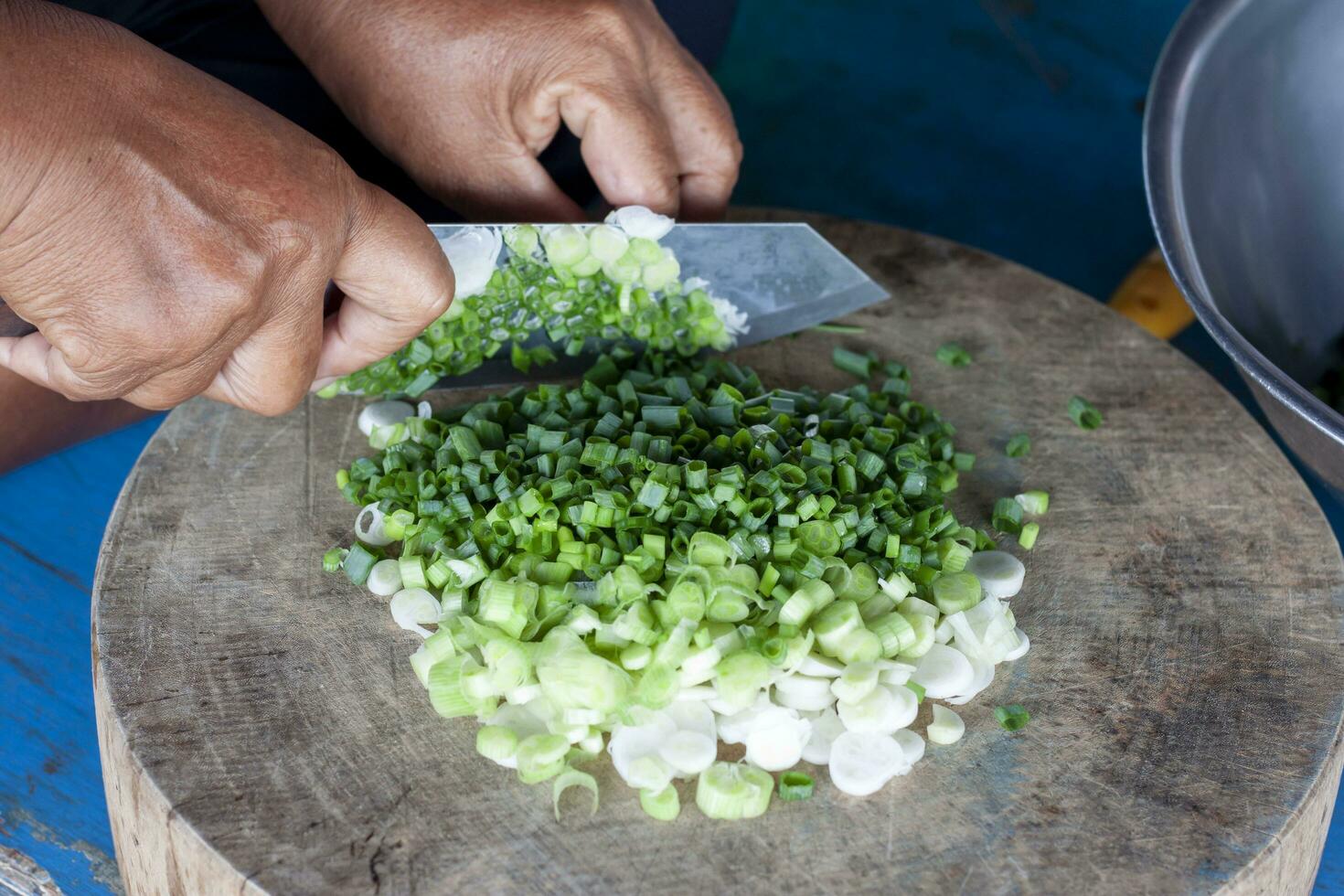 Hand of woman holding a knife to cut spring onion into slices on the wooden butcher in the kitchen to cook. photo