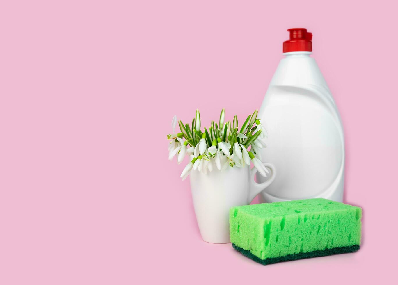 Detergent, kitchen sponge and spring flowers on a pink background. Cleaning concept. Banner. Copy space. Close-up. Selective focus. photo