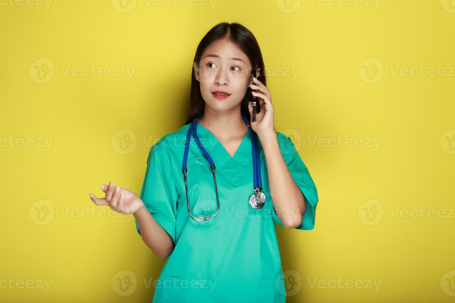 Portrait of a beautiful young woman in a yellow background, Asian woman poses with a cell phone while wearing a doctor's uniform and a stethoscope. photo