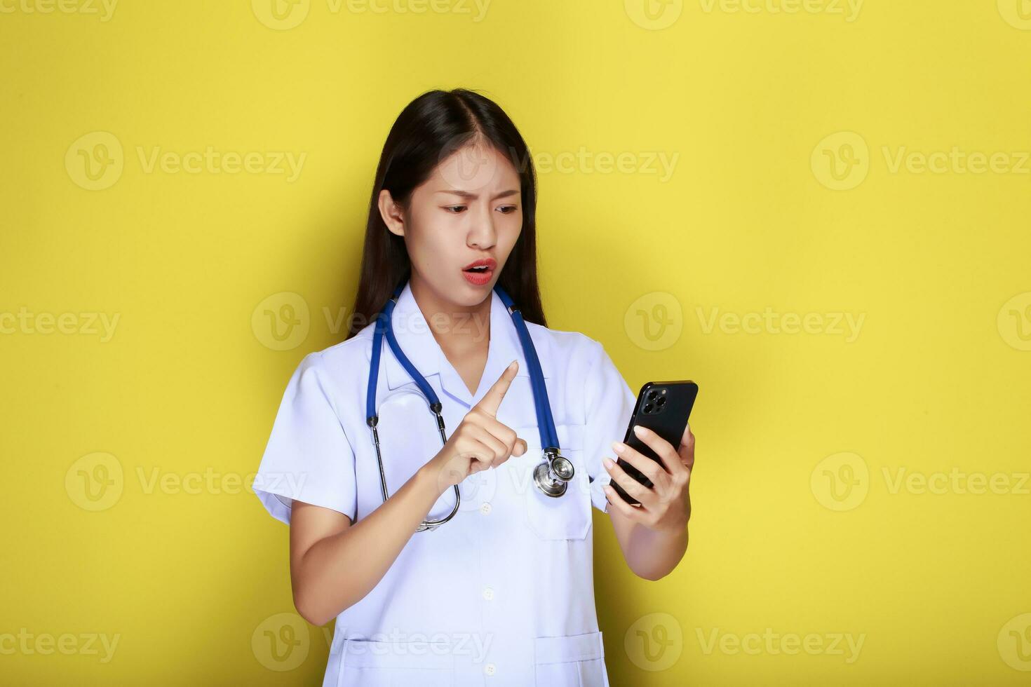 Portrait of a beautiful young woman in a yellow background, Asian woman poses with a cell phone while wearing a doctor's uniform and a stethoscope. photo
