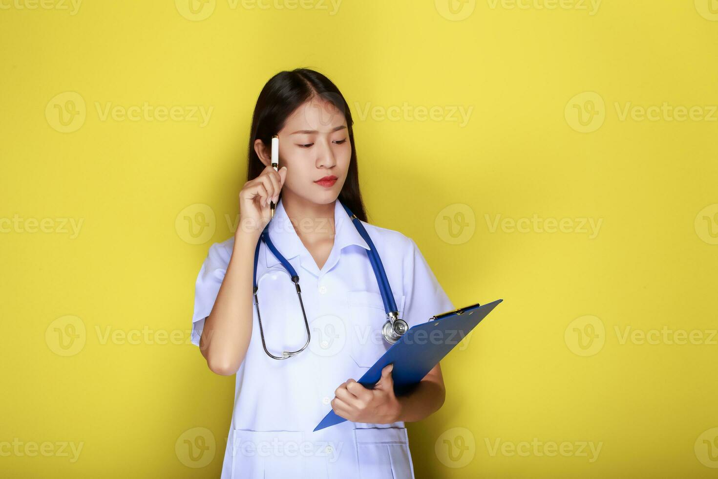 Beautiful young woman makes a thoughtful expression while wearing a doctor's uniform standing in front of a yellow background. photo