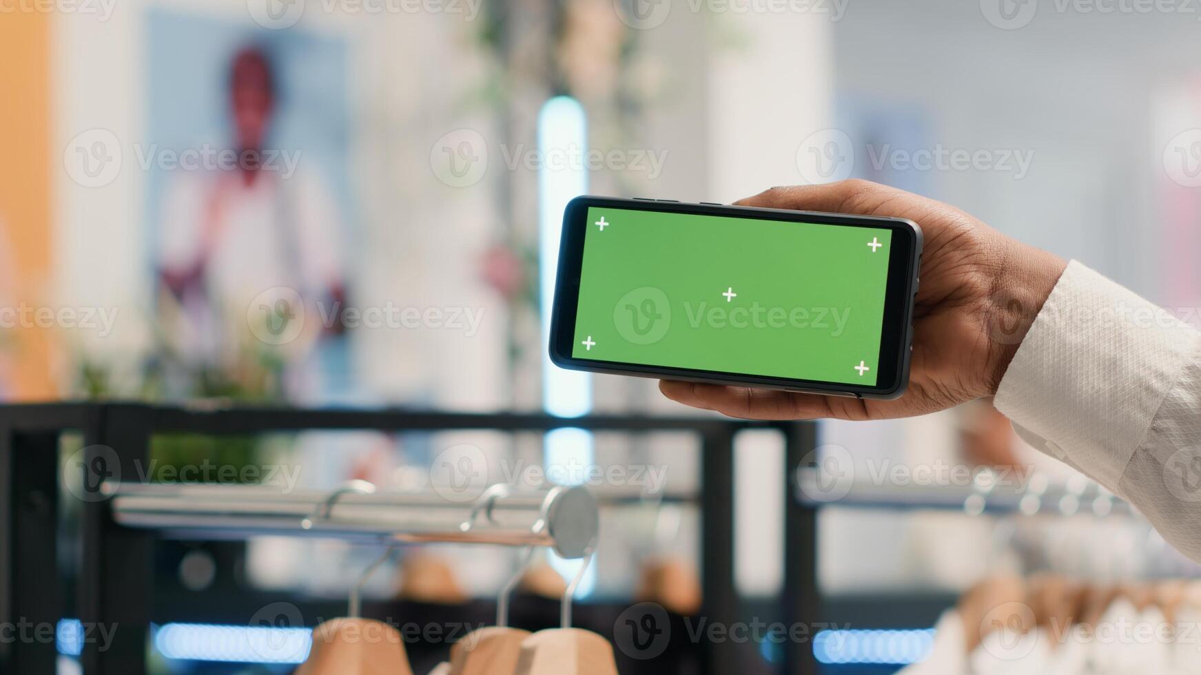 Customer in SH clothing shop holding green screen mobile phone, deciding what clothes to purchase. Client looking at new collection of garments in discount store using chroma key smartphone, close up photo