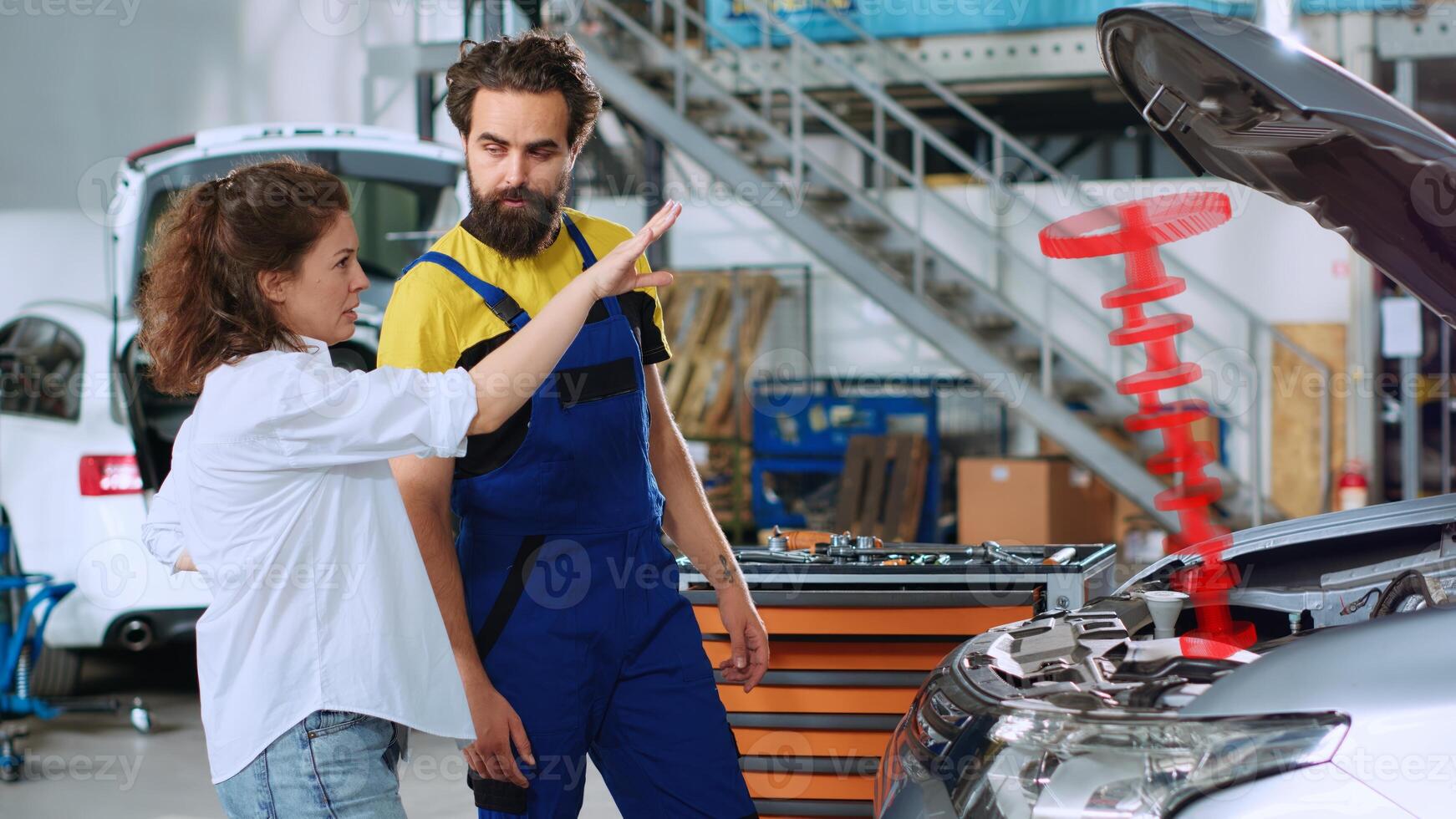 Serviceman in car service using holographic augmented reality to show customer defective vehicle piston. Hardworking garage employee using innovative AR tech to project automobile parts for woman photo