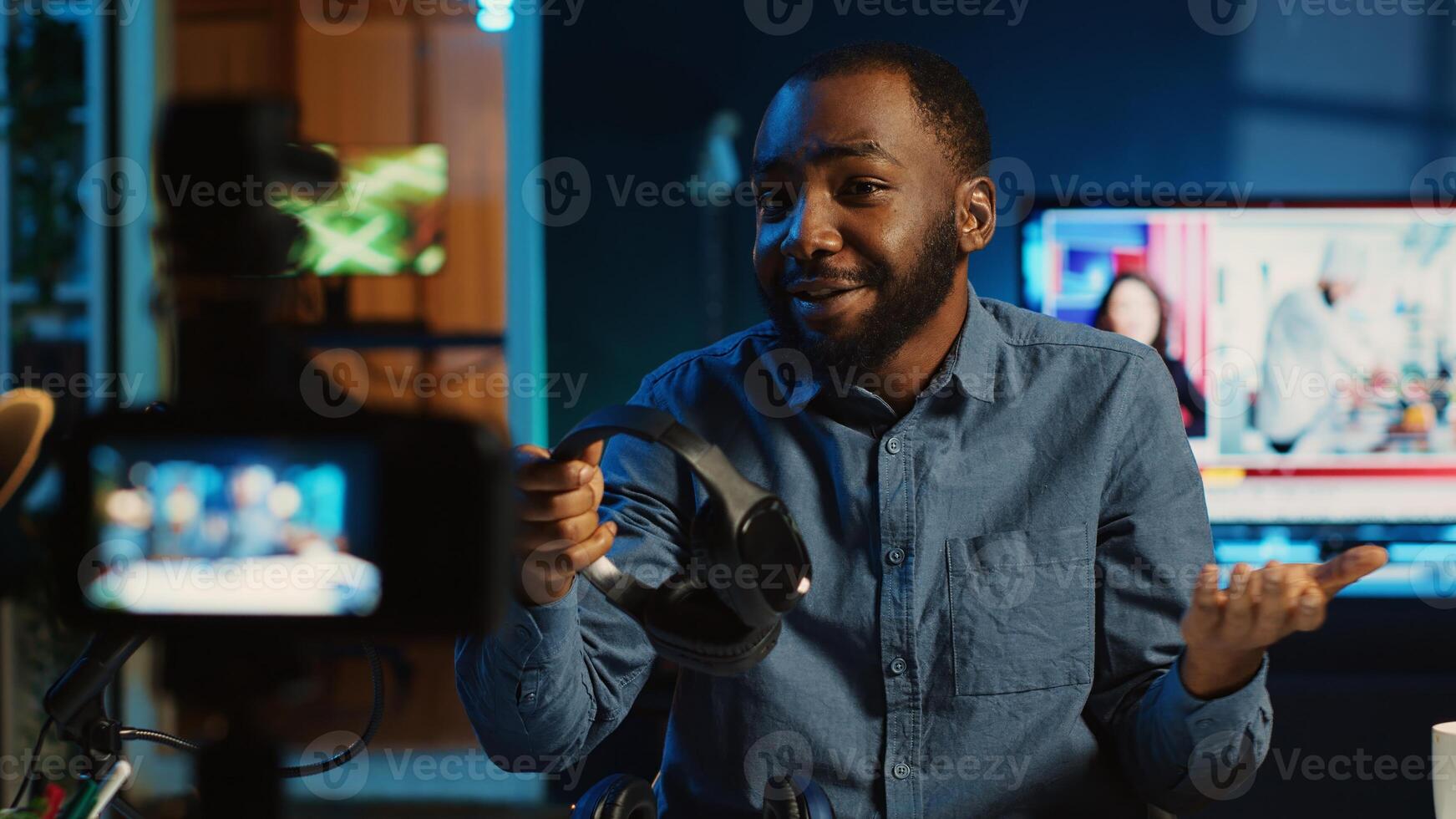 Content creator in dimly lit living room uses camera to film noise cancelling headphones review for online streaming platforms. Online star hosts internet show, unboxing music listening device photo