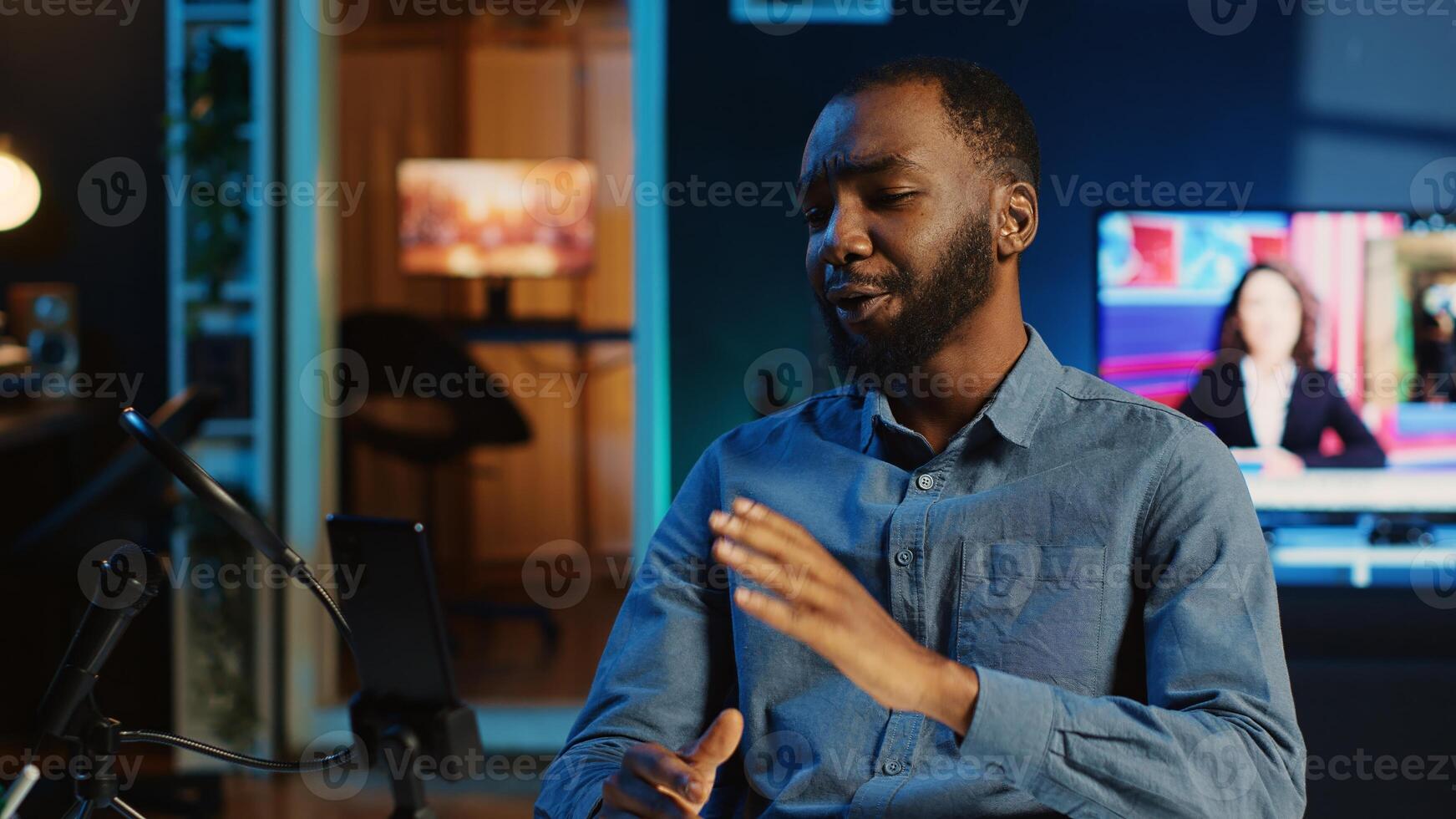 Content creator in dimly lit home studio using cellphone camera to film video for online streaming platforms. Influencer hosts q a session with audience using mobile phone photo