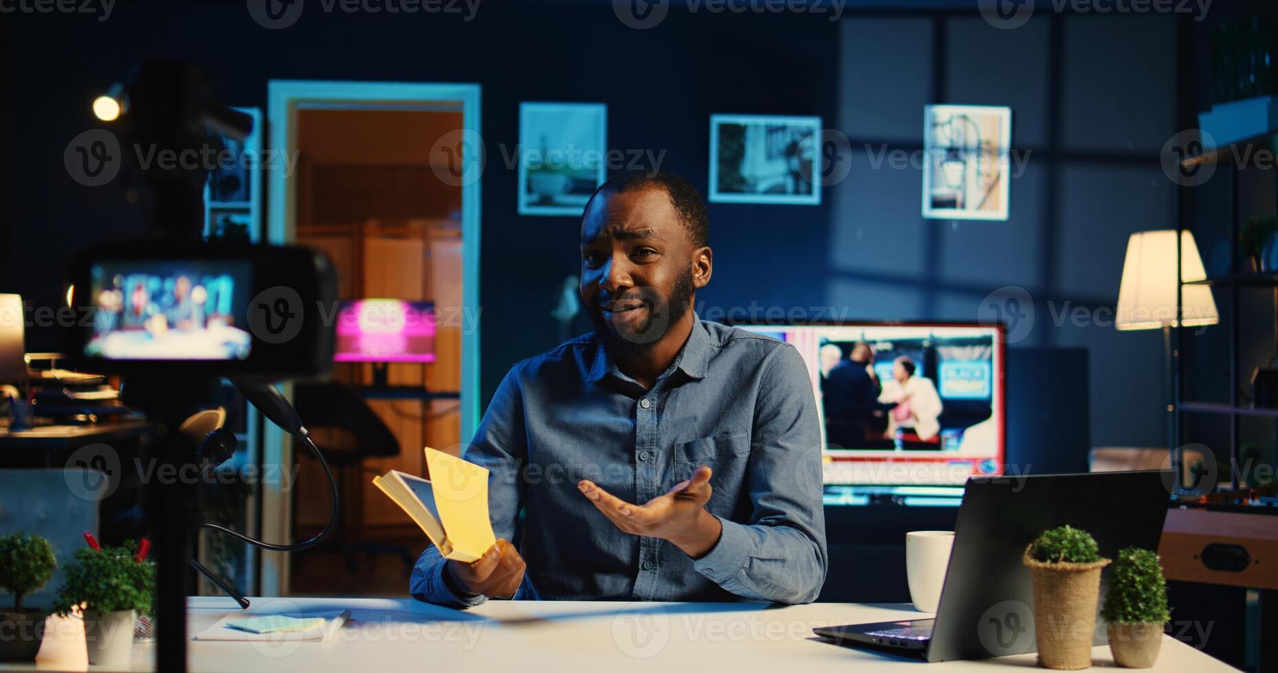 Smiling content creator films video review of book, presenting synopsis to audience in home studio. Media star sponsored by publisher to show new novel release to readers, handheld camera photo