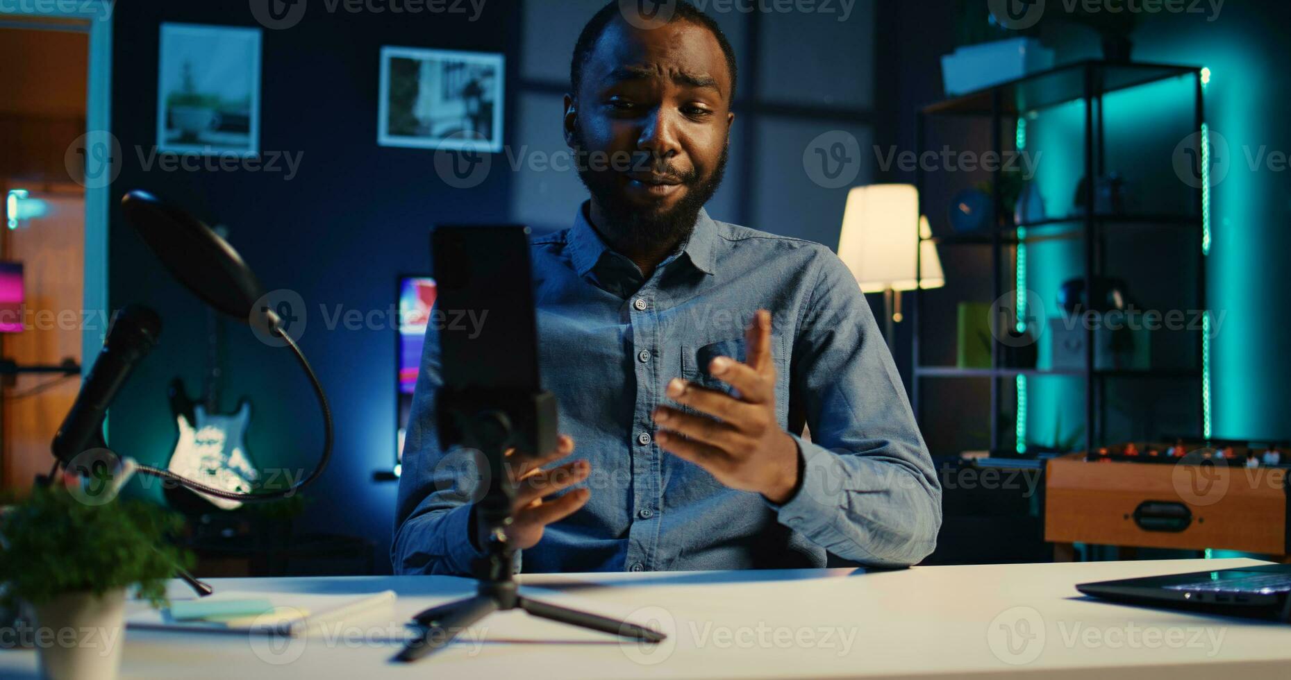 Content creator in dimly lit home studio using cellphone camera to film live broadcast for online streaming platforms. Internet star hosts q a session with audience using mobile phone photo