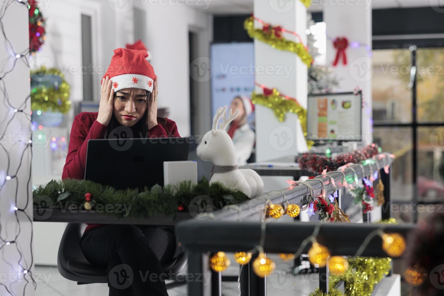 Overworked employee overwhelmed with stressful paperwork overload with deadline approaching before Christmas holiday season. Unhappy worker in festive ornate office getting fatigued from busy job photo