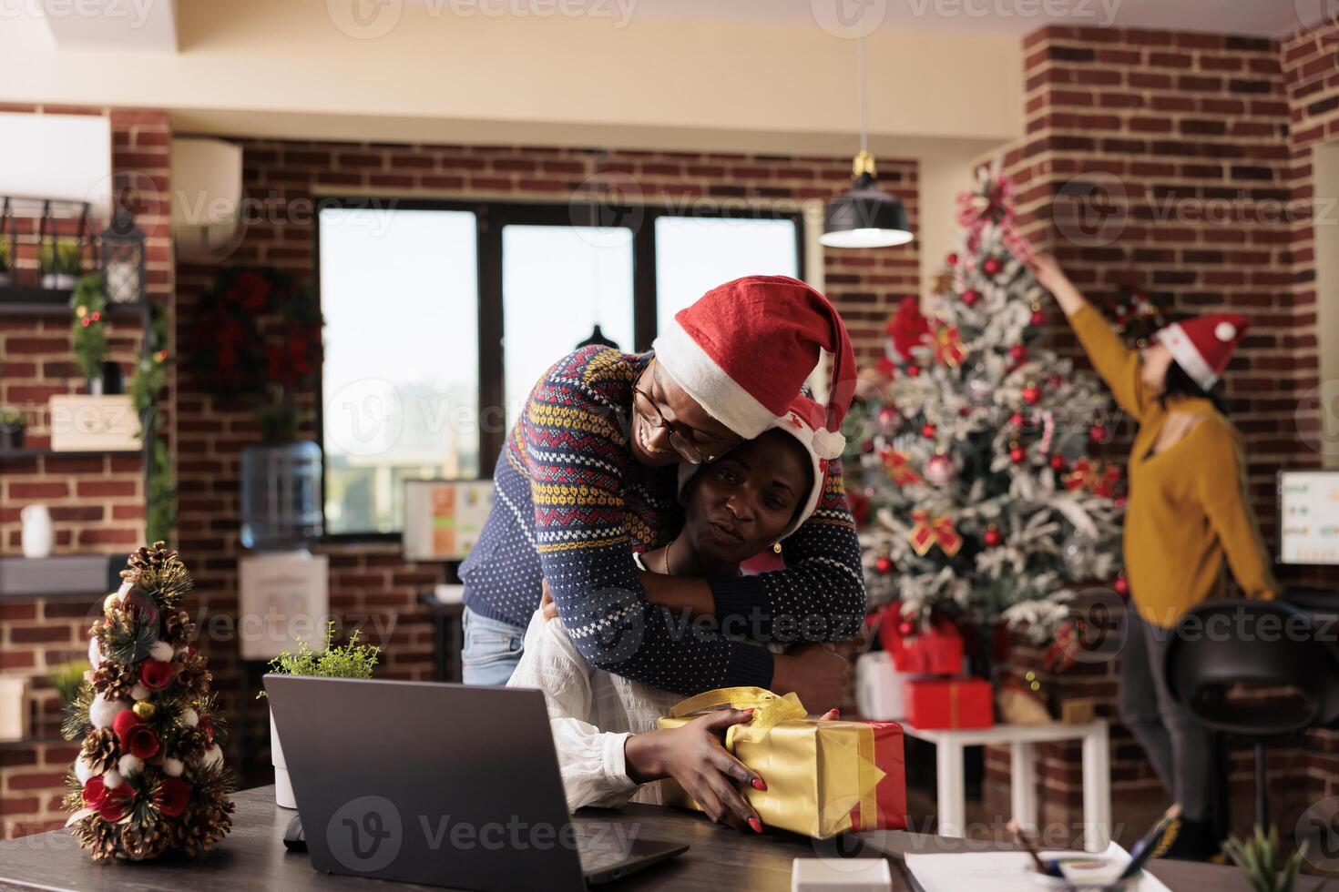 African american office employee hugging colleague while greeting with christmas gift. Company coworkers embracing while sharing xmas presents and spreading holiday atmosphere photo
