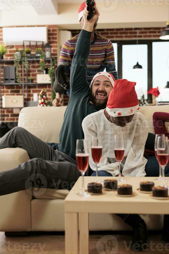 Happy man employee with joystick winning video game while celebrating christmas with colleagues in office. Excited company worker holding gamepad while enjoying new year corporate party photo