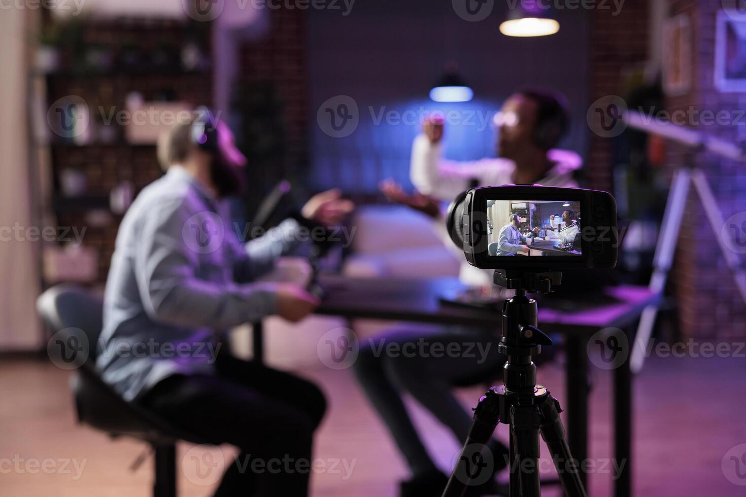 Focus shot on professional camera used to record podcast show with presenter and guest discussing in blurry background. Equipment in home studio used for live streaming broadcast photo