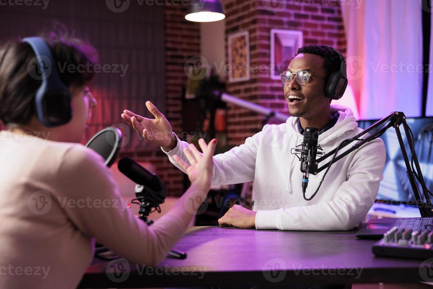 African american podcast host discussing with guest during live broadcast for social media website, being surprised by her knowledge. Internet star chatting with woman during online stream photo