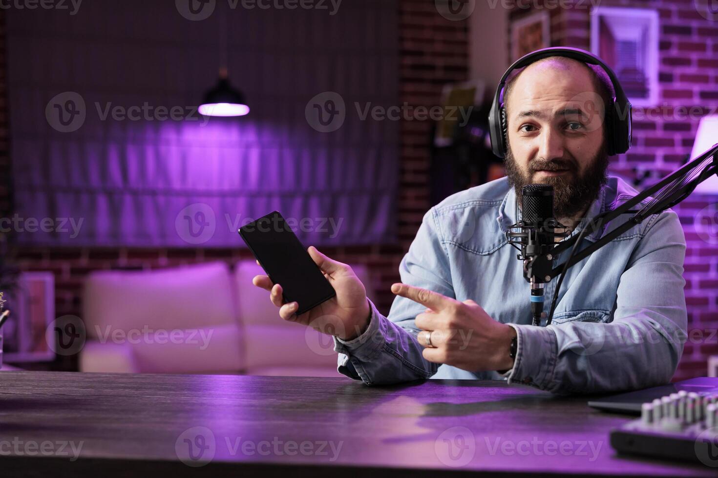 Portrait of tech vlogger reviewing newly released smartphone in rgb lights living room studio. Entertaining content creator filming technology channel episode using professional video tools photo