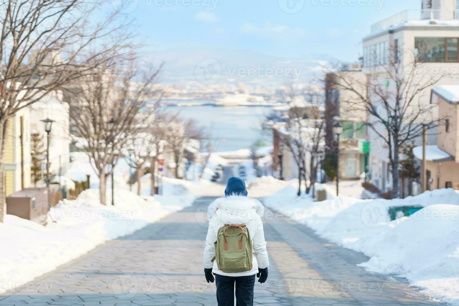 Woman tourist Visiting in Hakodate, Traveler in Sweater sightseeing Hachiman Zaka Slope with Snow in winter. landmark and popular for attractions in Hokkaido, Japan. Travel and Vacation concept photo