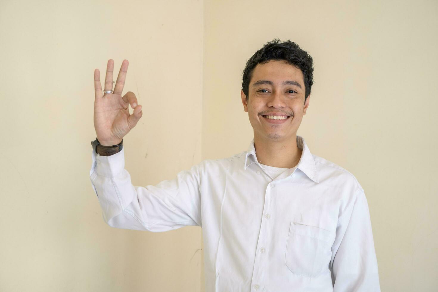 Young Indonesian curly man wear white clothes with ok pose. photo