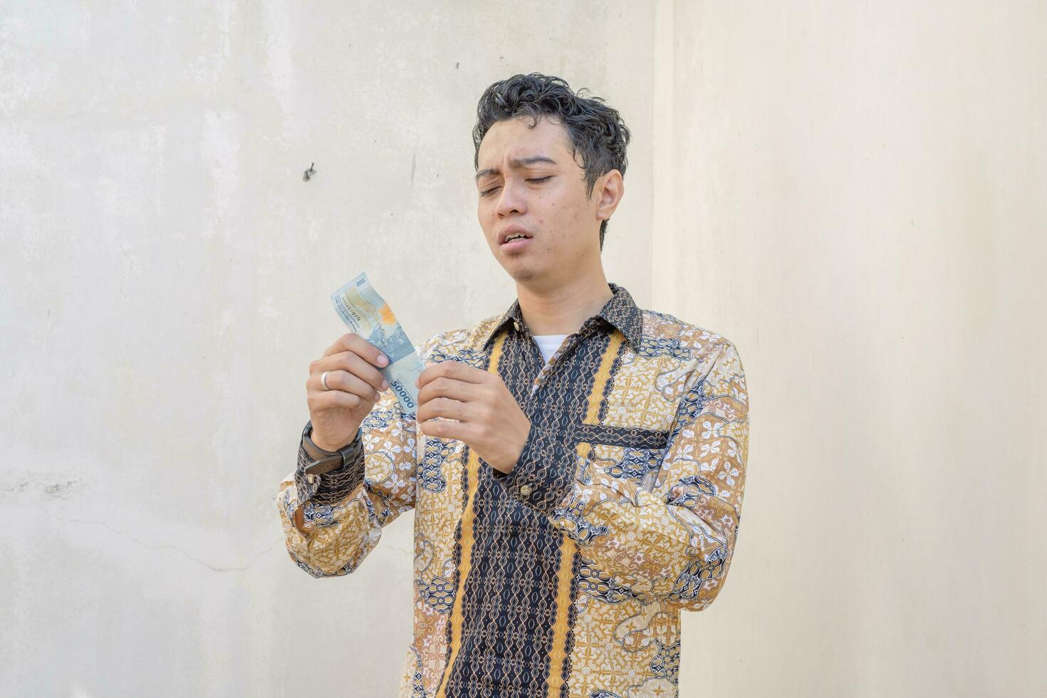 Young Indonesian wear batik traditional culture of Indonesia sad when look the money. photo