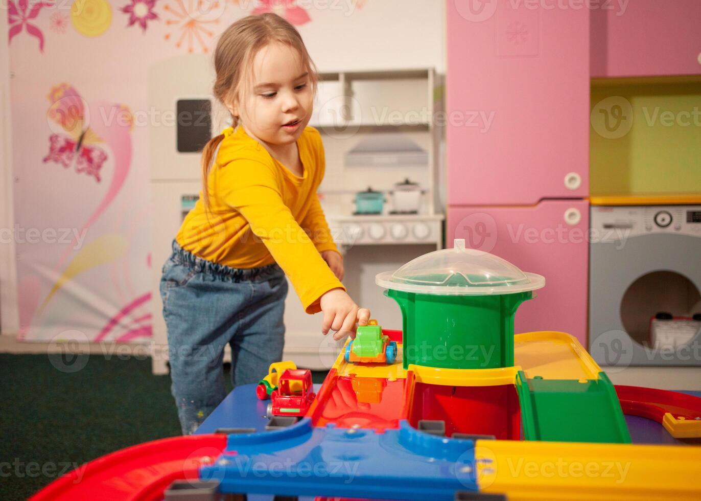 child in kindergarten, playroom, playing with toys, learning. Plays with car, race track, constructor. Contented. photo