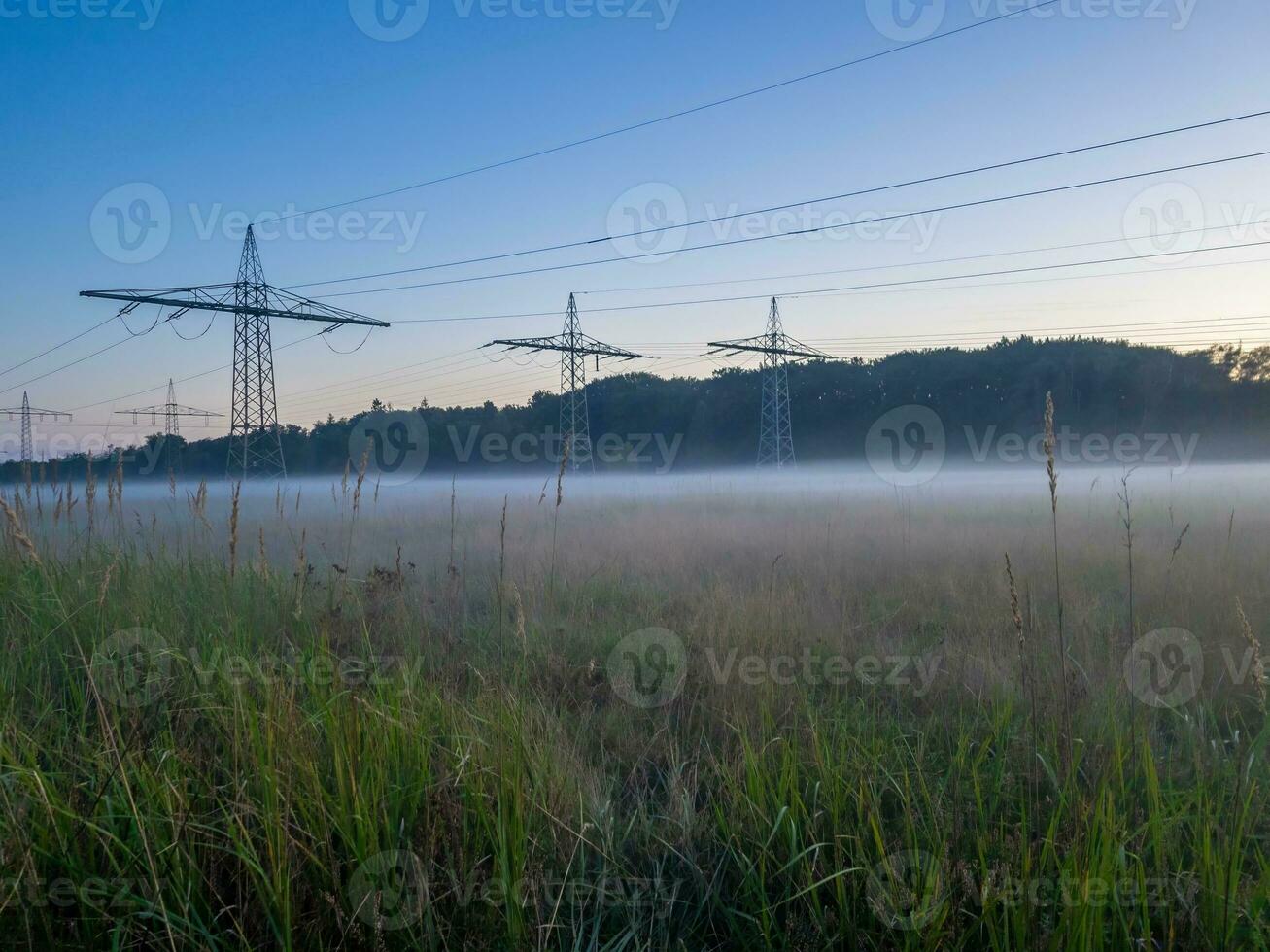 Panoramic image of a meadow with high-voltage pylons and ground fog in autumn photo