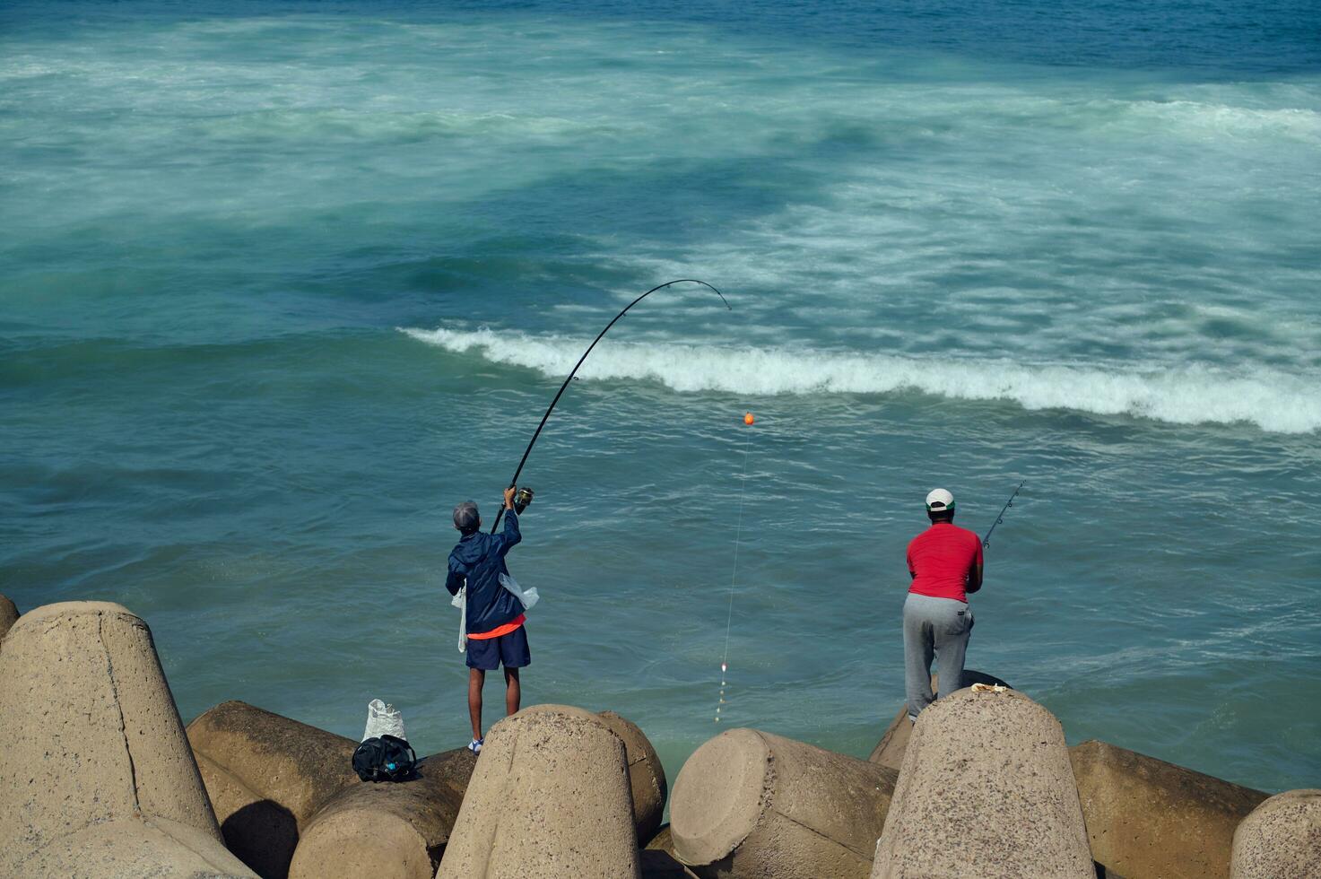 posterior ver de irreconocible personas - pescador en pie en el costa en rompeolas y pescar en atlántico océano. gente. ocio. pasatiempo foto