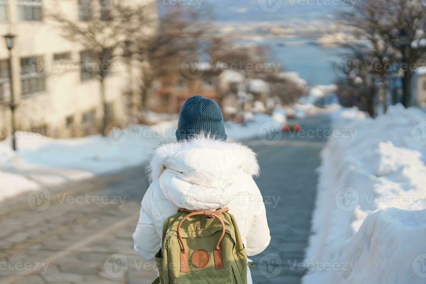 Woman tourist Visiting in Hakodate, Traveler in Sweater sightseeing Hachiman Zaka Slope with Snow in winter. landmark and popular for attractions in Hokkaido, Japan. Travel and Vacation concept photo