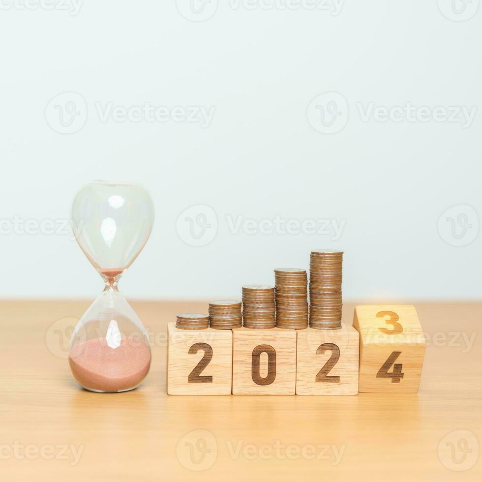 Happy New Year with sandglass and flipping 2023 change to 2024 block. Resolution, Goals, Plan, Action, Money Saving, Retirement fund, Pension, Investment and Financial concept photo