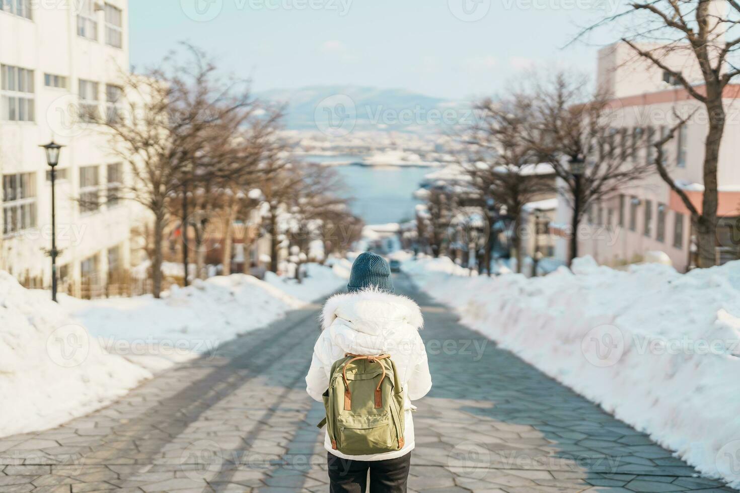 Woman tourist Visiting in Hakodate, Traveler in Sweater sightseeing Hachiman Zaka Slope with Snow in winter. landmark and popular for attractions in Hokkaido, Japan. Travel and Vacation concept photo