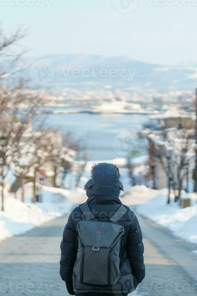 Man tourist Visiting in Hakodate, Traveler in Sweater sightseeing Hachiman Zaka Slope with Snow in winter. landmark and popular for attractions in Hokkaido, Japan. Travel and Vacation concept photo